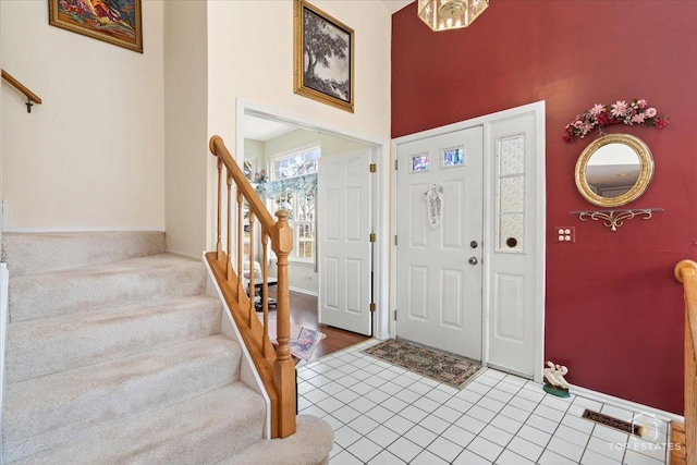 tiled foyer entrance featuring stairs, a high ceiling, and baseboards