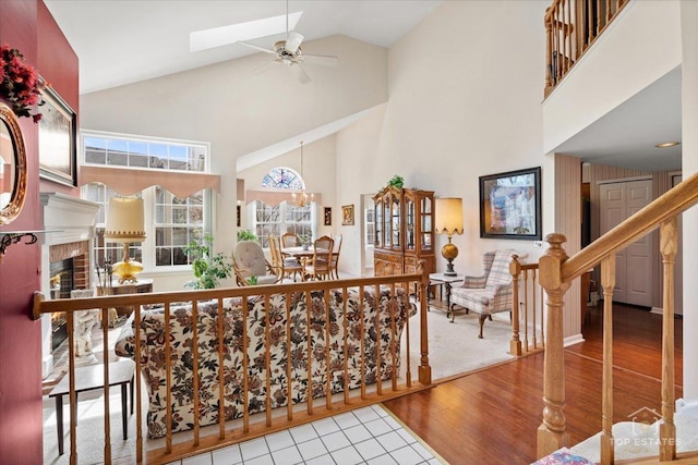 living area with ceiling fan, a brick fireplace, wood finished floors, stairway, and high vaulted ceiling