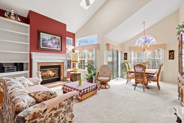 carpeted living room with a healthy amount of sunlight, high vaulted ceiling, a fireplace, and a notable chandelier