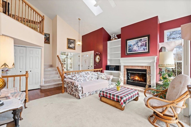 carpeted living room featuring stairs, wood finished floors, a fireplace, high vaulted ceiling, and a skylight