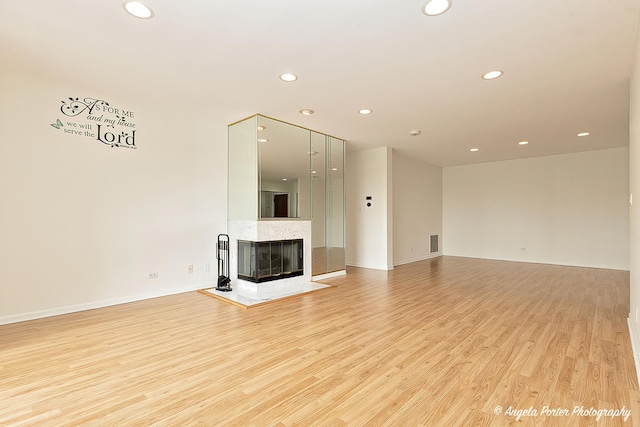 unfurnished living room featuring recessed lighting, a high end fireplace, and light wood-type flooring