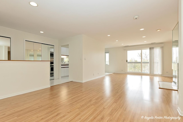 unfurnished living room with recessed lighting, baseboards, a sink, and light wood-type flooring