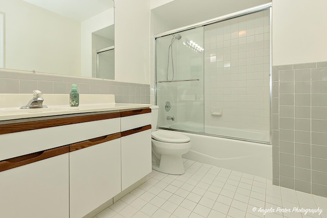 bathroom with tile walls, bath / shower combo with glass door, vanity, tile patterned floors, and toilet