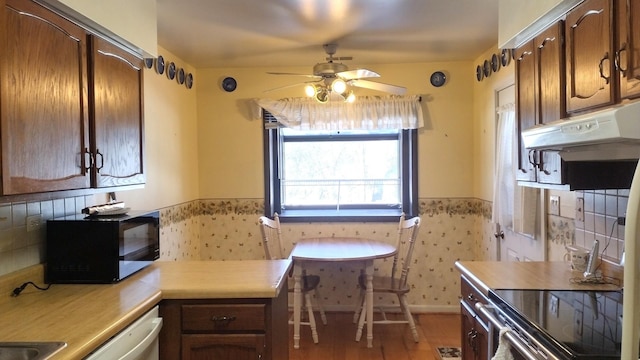 kitchen featuring black microwave, brown cabinets, a sink, freestanding refrigerator, and light wood finished floors