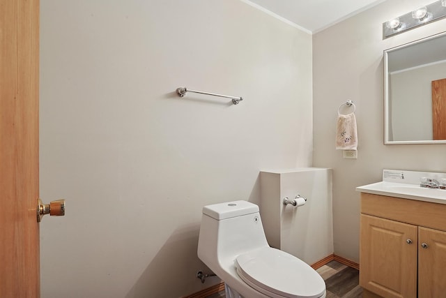 half bathroom featuring toilet, vanity, wood finished floors, and crown molding