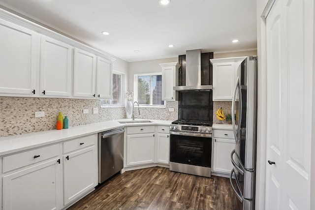 kitchen with wall chimney exhaust hood, appliances with stainless steel finishes, a sink, white cabinets, and dark wood finished floors
