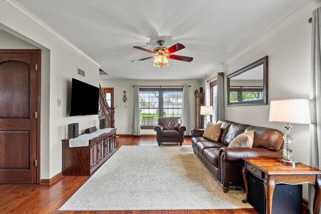 living area with visible vents, ornamental molding, wood finished floors, baseboards, and ceiling fan