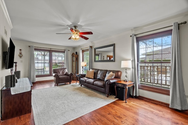living area with a ceiling fan, visible vents, baseboards, light wood-style floors, and ornamental molding