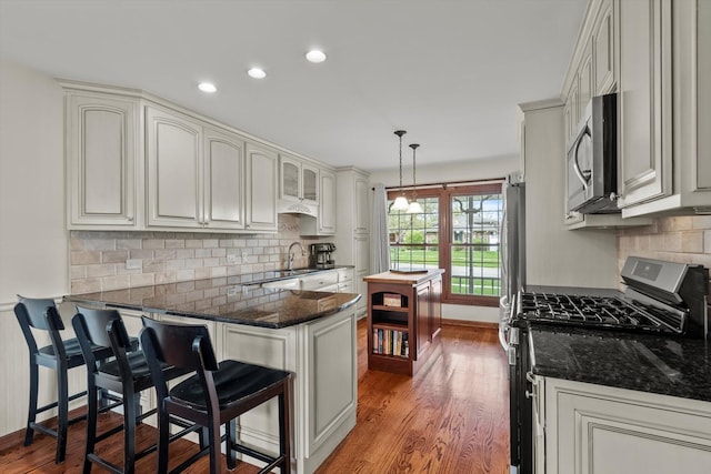 kitchen with decorative light fixtures, wood finished floors, a peninsula, a breakfast bar, and stainless steel appliances
