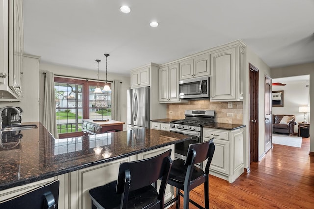 kitchen with appliances with stainless steel finishes, a sink, light wood finished floors, a peninsula, and decorative backsplash