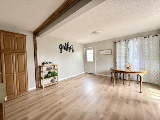 interior space with a textured ceiling, baseboards, light wood finished floors, and beam ceiling