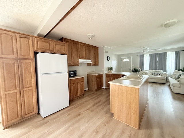kitchen with a sink, a textured ceiling, freestanding refrigerator, light wood-type flooring, and under cabinet range hood