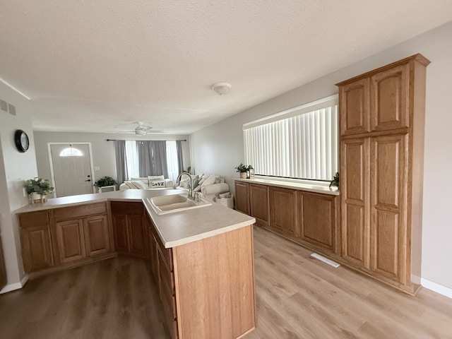 kitchen with a sink, light wood-style floors, light countertops, a peninsula, and a ceiling fan
