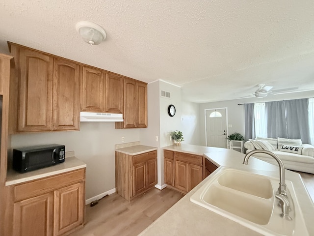 kitchen with black microwave, a sink, a textured ceiling, light wood-type flooring, and under cabinet range hood