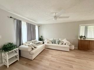 living room featuring light wood-type flooring, baseboards, ceiling fan, and a healthy amount of sunlight