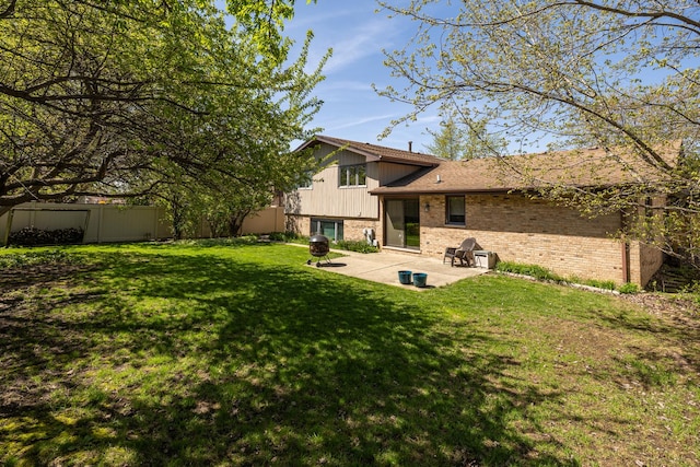 rear view of house featuring a yard, brick siding, fence, and a patio area