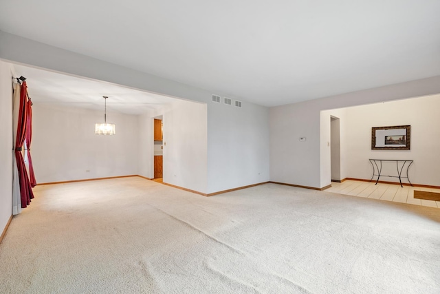 carpeted empty room with baseboards, visible vents, and a notable chandelier