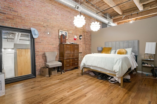 bedroom with brick wall, visible vents, wood finished floors, and a towering ceiling