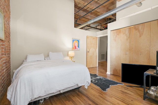 bedroom featuring visible vents, a closet, a towering ceiling, wood finished floors, and brick wall
