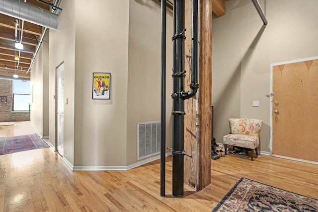 interior space featuring baseboards, a towering ceiling, wood finished floors, and visible vents