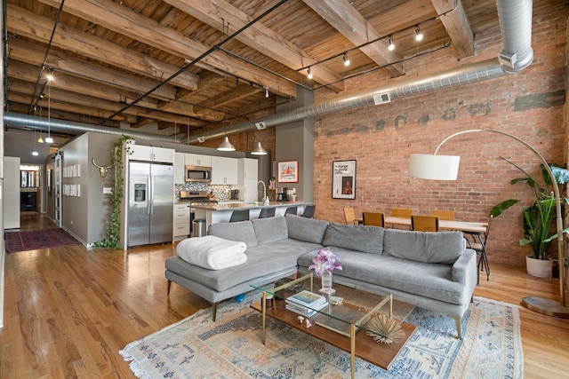 living room featuring track lighting, light wood-style floors, brick wall, and wooden ceiling