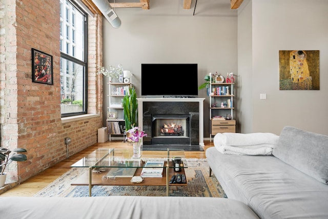living area featuring plenty of natural light, a fireplace with flush hearth, wood finished floors, and brick wall