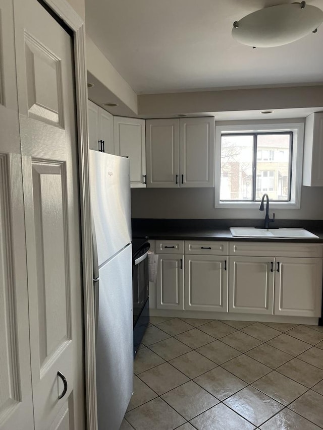 kitchen featuring light tile patterned flooring, dark countertops, a sink, freestanding refrigerator, and black range with electric cooktop