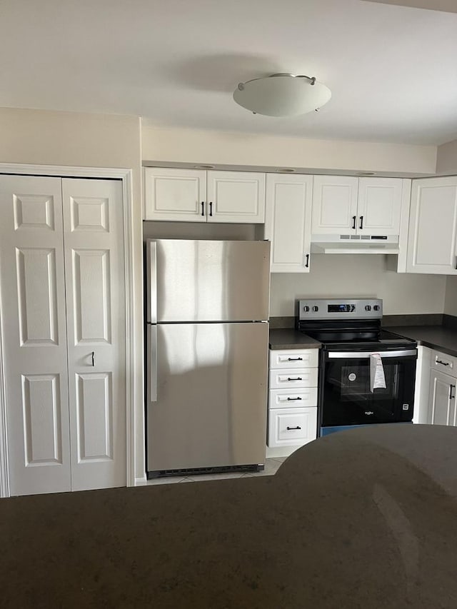 kitchen featuring freestanding refrigerator, dark countertops, range with electric stovetop, under cabinet range hood, and white cabinets