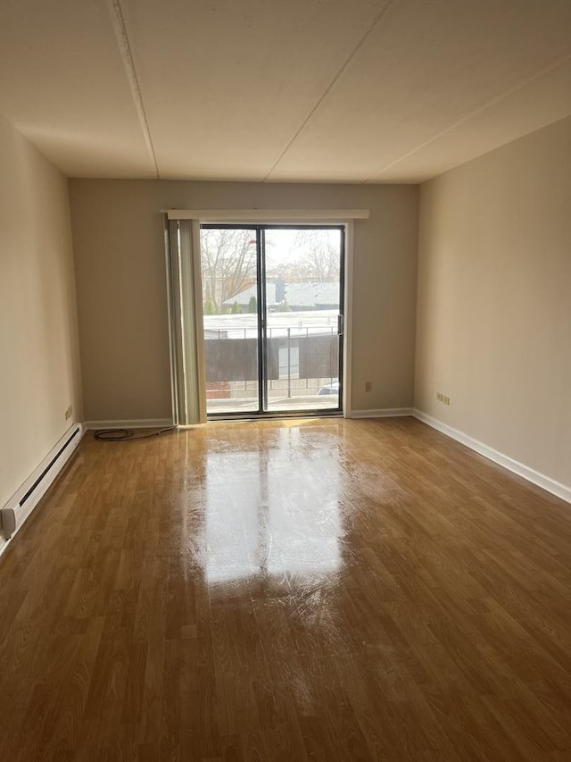 empty room featuring baseboards, baseboard heating, and wood finished floors