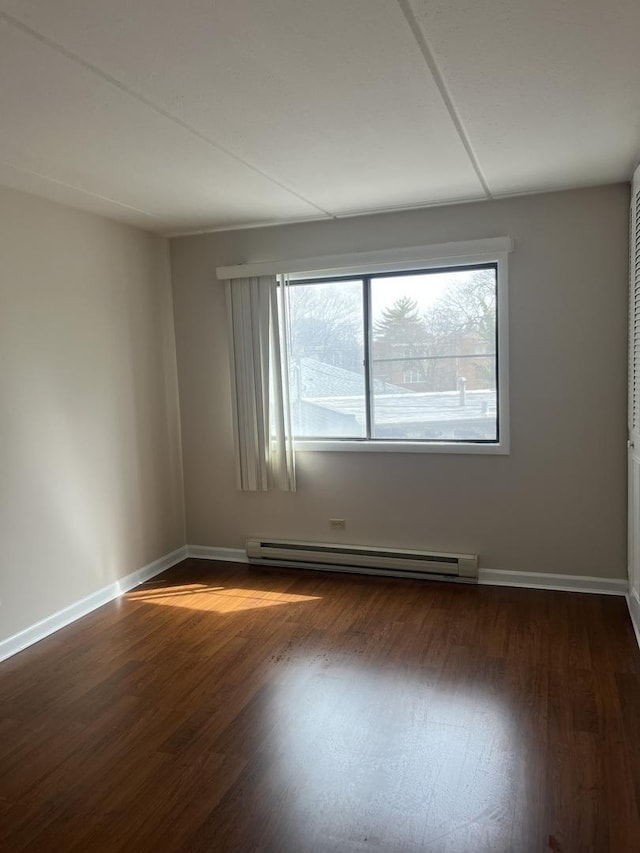 empty room with wood finished floors, baseboard heating, and a healthy amount of sunlight