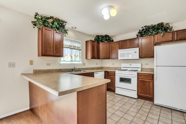 kitchen featuring a kitchen bar, a sink, light countertops, a peninsula, and white appliances
