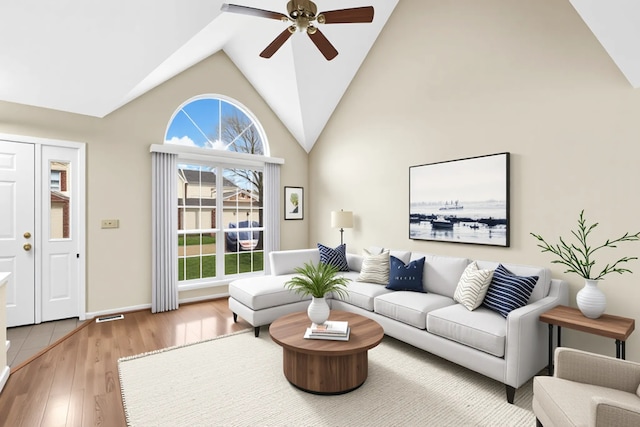 living area with visible vents, wood finished floors, baseboards, ceiling fan, and high vaulted ceiling