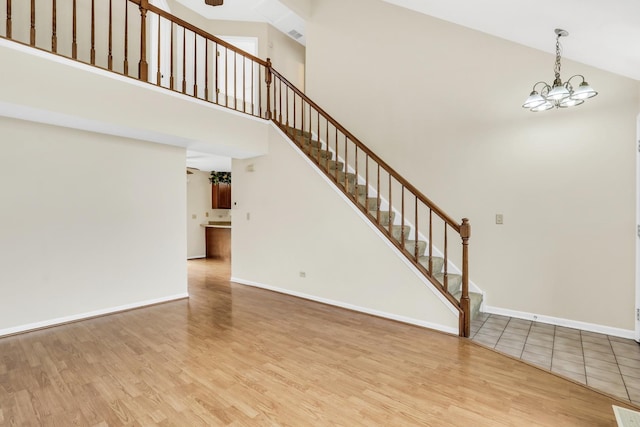unfurnished living room with wood finished floors, high vaulted ceiling, baseboards, an inviting chandelier, and stairs