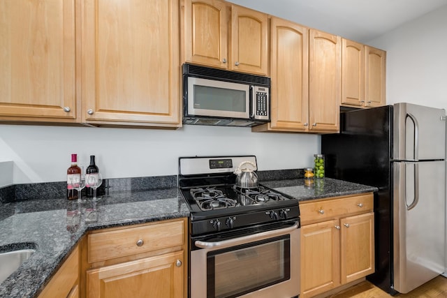 kitchen featuring light brown cabinetry, stainless steel appliances, and dark stone countertops