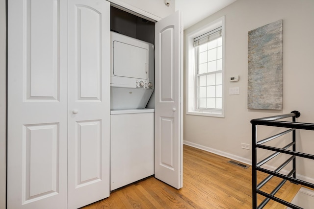 washroom with laundry area, stacked washer and clothes dryer, visible vents, light wood-style floors, and baseboards