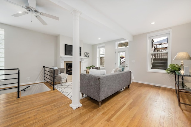living room featuring ceiling fan, visible vents, a fireplace, baseboards, and light wood-style floors