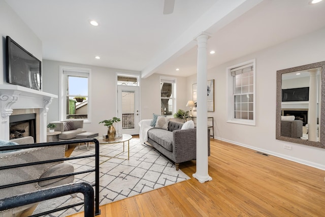 living area with visible vents, a fireplace, baseboards, ornate columns, and light wood-type flooring