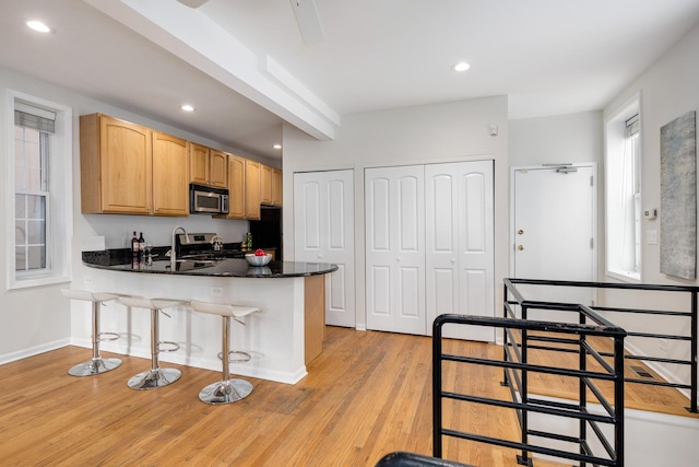 kitchen featuring appliances with stainless steel finishes, light wood-style floors, a kitchen breakfast bar, a peninsula, and recessed lighting