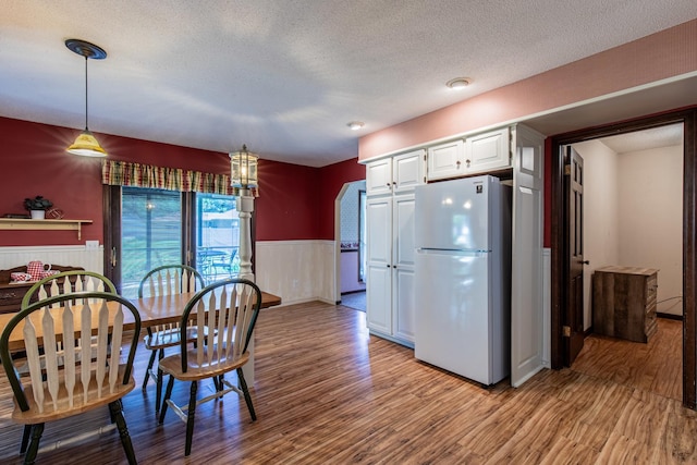 11 N Beech St, Princeton, IL 61356 - kitchen with freestanding refrigerator, light wood-style flooring, a wainscoted wall, a textured ceiling, and white cabinets