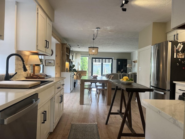 kitchen featuring a sink, stainless steel appliances, white cabinetry, wood finished floors, and backsplash