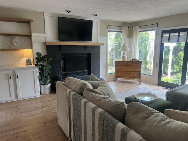 living area featuring a textured ceiling, visible vents, a brick fireplace, light wood-type flooring, and a decorative wall