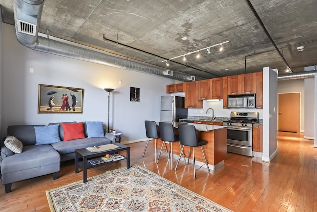 kitchen with stainless steel appliances, a kitchen bar, light wood-style flooring, brown cabinetry, and baseboards