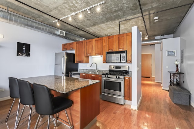 kitchen with stainless steel appliances, rail lighting, brown cabinetry, a kitchen bar, and light wood-style flooring