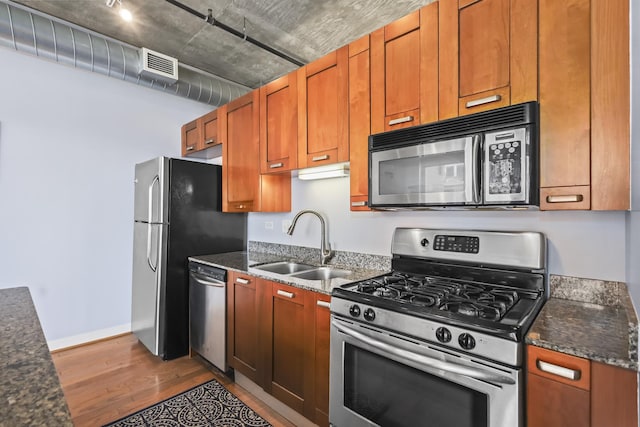 kitchen with appliances with stainless steel finishes, a sink, wood finished floors, dark stone countertops, and baseboards