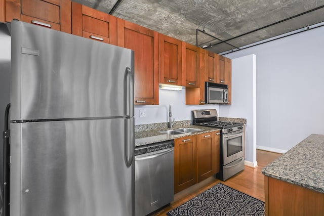 kitchen featuring stainless steel appliances, a sink, wood finished floors, and dark stone countertops