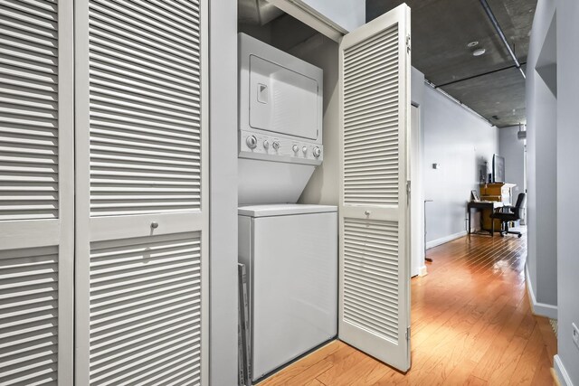 laundry room with stacked washer and clothes dryer, an office area, light wood-type flooring, and baseboards