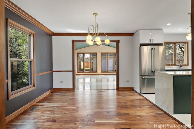 unfurnished dining area featuring baseboards, a sink, light wood finished floors, and crown molding