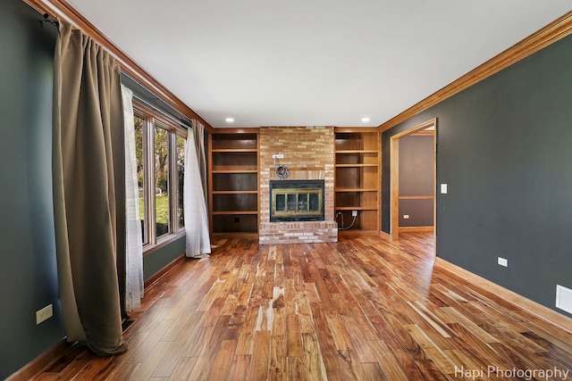 unfurnished living room featuring wood-type flooring, crown molding, built in features, a brick fireplace, and baseboards