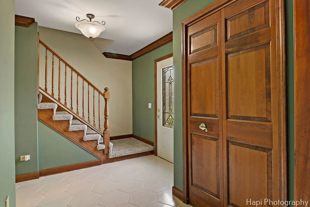 foyer entrance with baseboards, crown molding, light tile patterned flooring, and stairway