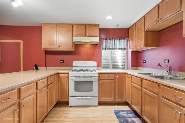 kitchen featuring white gas range, light countertops, a sink, light wood-style floors, and under cabinet range hood